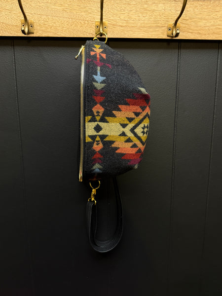 Colorful patterned pouch hanging on a wooden rack against a black wall.
