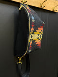 Colorful geometric-patterned pouch with a black interior hanging on a hook against a dark wall.