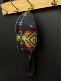 Colorful patterned pouch hanging on a wooden coat rack against a black wall.