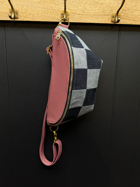 Checkered bag with pink Leather top and  strap hanging on a wooden hook against a black wall.