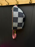 Checkered pouch with pink strap hanging on a wooden rack against a dark wall.