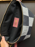 Checkered pouch with a pink label held by a hand against a neutral background
