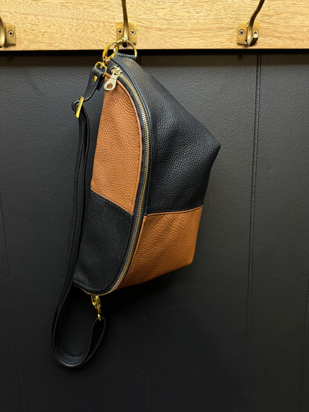Black and brown leather bag hanging on a wooden hook against a dark wall.