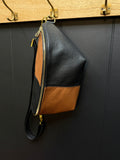 Black and brown leather handbag with gold zipper on a dark wall.