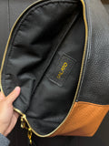 Close-up of a black leather bag with a visible brand logo, held open by a hand.