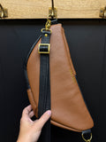 Brown leather bag with black strap held by a hand against a dark background
