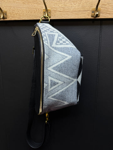 Grey and white geometric patterned bag with gold zipper  and black leather on a black background