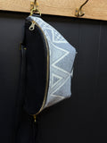 Grey and white geometric patterned pouch with black Leather hanging on a wooden surface.