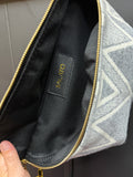 Gray geometric-patterned pouch with gold zipper and visible brand label on black interior.